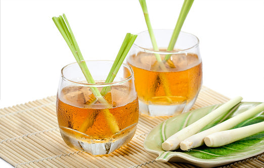 Two glasses of lemongrass tea with fresh lemongrass stalks on a bamboo mat and plate